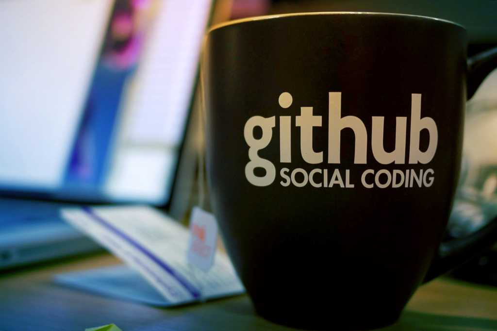 A 'GitHub social coding' mug sits in a desktop workspace.